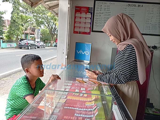 BELI VOUCHER: Penjaga konter handphone di Dusun Krajan, Desa Yosomulyo, Kecamatan Gambiran melayani pelanggan kemarin (11/5). (Lugas Rumpakadi/RadarBanyuwangi.id)
